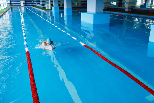 Image on top of sportive man in blue cap swimming on path in pool under water