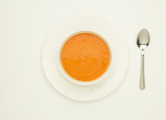 WHITE BOWL CONTAINING TOMATO SOUP ON WHITE PLATE WITH SPOON
