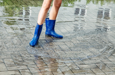 girl in rubber boots standing in a puddle after a rain