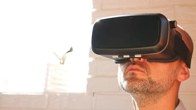 Man using virtual reality headset at office. Bearded man uses VR headset display for game