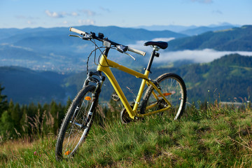 Naklejka na ściany i meble Yellow bike stands on a hill against a beautiful landscape of the powerful Carpathian mountains wrapped in smoke