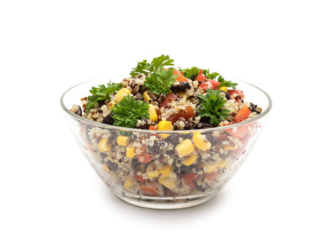Side view of glass bowl with quinoa salad with red pepper, corn, tomato and black beans, topped with parsley and isolated on white background