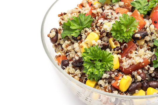 Close up of glass bowl with quinoa salad with red pepper, corn, tomato and black beans, topped with parsley and isolated on white background