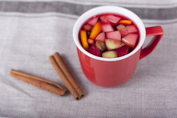 Чай с фруктами в красной чашке на льняной скатерти крупным планом. Палочки корицы 
