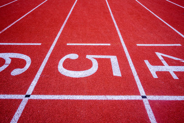 red surface running racetrack with white lines and number in outdoor stadium