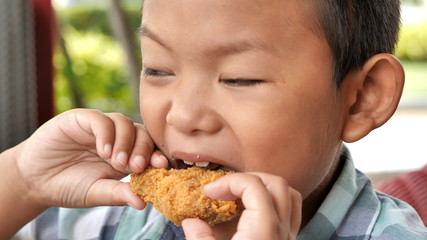 Cute asian boy are happy eating fried chicken leg in restaurant