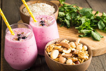 Glasses of berry smoothie with nuts, mint, blueberry, blackberry, raspberry, and yogurt on wooden table. Weight loss and diet concept. 