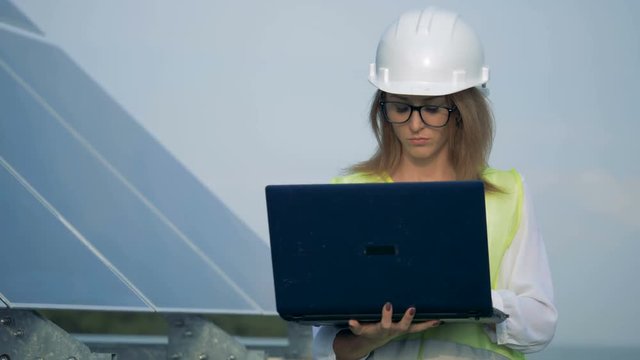 Female engineer is walking with her laptop near a solar battery