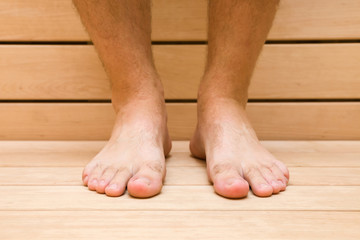 Young man sitting in the wooden sauna. Barefoot close up. Care about healthy body. Relax time. Front view.