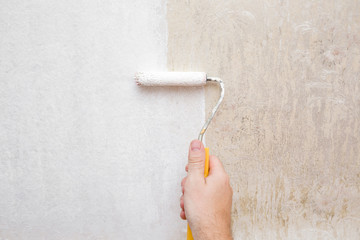 Man's hand painting old, dirty wallpaper in white color with paint roller. Renewal of old things....