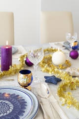 Obraz na płótnie Canvas Close-up of a decorated dining table with burning candles, sterling cutlery, crystal glasses, colorful christmas balls and gold tinsel