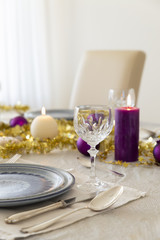 Close-up of a decorated dining table with burning candles, sterling cutlery, crystal glasses, colorful christmas balls and gold tinsel