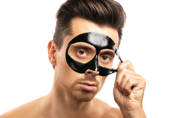 Young guy with a black charcoal mask on his face on white background.