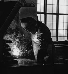 Welder at the factory in a welding mask welds metal parts, welding and sparks, black and white, welding holder