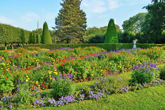Lush flowerbed with blooming flowers in the background of hedges and neatly trimmed trees in the beautiful public city garden at summer sunny day