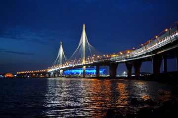 Panorama of the cable-stayed bridge of the high-speed road in St. Petersburg over the Neva river and the Gulf of Finland and the football stadium Zenit arena with blue illumination at night. Russia