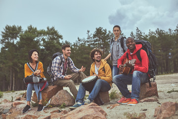 Song time. Portrait of group of friends spending time on the beach playing drum, guitar and singing