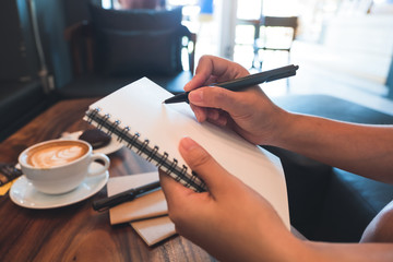 Closeup image of a woman's hands holding and writing down on a white blank notebook in cafe