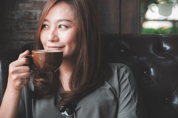 Closeup image of a beautiful Asian woman holding and drinking hot coffee with feeling good in vintage cafe