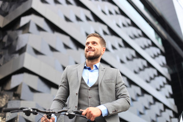 Confident young businessman walking with bicycle on the street in town.