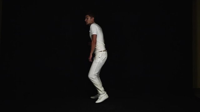 Energetic young, slim, good-looking charismatic man with big blue eyes and modern haircut dressed in white t-shirt and pants, starts running towards camera on black background.