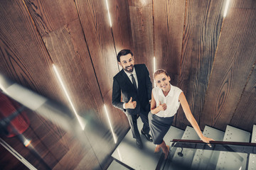 Full length top view portrait of cheerful lady and happy male employer expressing symbol cool with hand while locating indoor