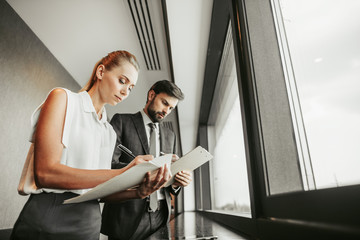 Low angle portrait of concentrated female and serene unshaven male employer writing in document
