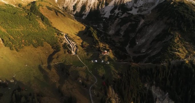 Cinematic view of alps mountain ridge and summit peak Zimba, Austria during sunrise. Drone tilting up filming hut cabin, rocky mountains and green valley.