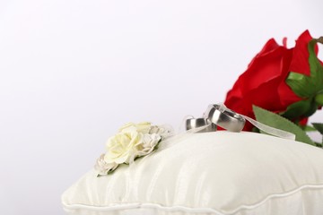 wedding rings - wedding rings on a white silk pillow with red roses in the background