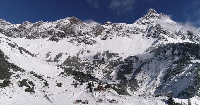 Aerial winter view of alps mountains and cabin hut in Austria. Drone rising up during beautiful clear and sunny winter day. Zimba peak and mountain ridge background