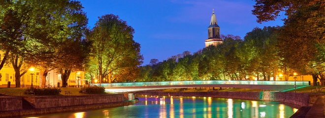  The night panoramic view of Aura river in Turku, Finland with a clock tower of cathedral and...