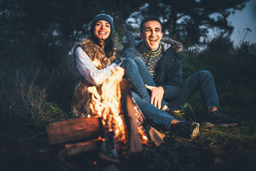 Pretty couple relaxing near bonfire in the forest at evening time