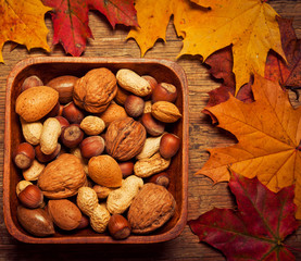 various kinds of nuts - dried fruit - hazelnuts, peanuts, walnuts, over wooden background with autumn leaf