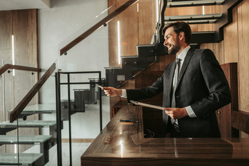 Side view cheerful bearded receptionist holding plastic card and clipboard with information in...