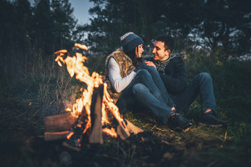 Pretty couple relaxing near bonfire in the forest at evening time