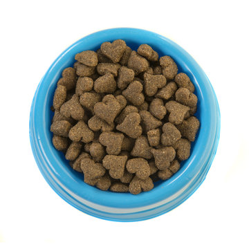 Blue round feeding bowl with dark brown heart shaped dog or cat kibble seen from above isolated on a white background