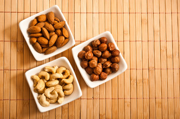 three white bowl with almonds, cashews and hazelnuts on bamboos background with copy space