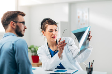 Portrait of Woman Doctor at her Medical Office Looking at X-Ray with Patient
