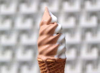 Melting Vanilla and Chocolate Flavors Soft Serve Ice Cream Cone with Blurred Modern Pattern Concrete Wall in Background 
