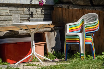 The sun is shining on friendly colored stacked plastic garden chairs and a table in a garden