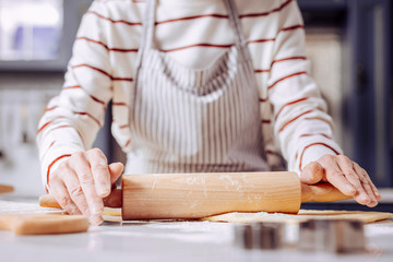Obraz premium Using rolling pin. Careful enthusiastic aged woman standing next to the table and touching the rolling pin while making tasty cookies