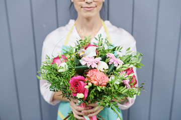 Mid section portrait of  female florist holding beautiful rose bouquet  posing by grey wooden wall, copy space