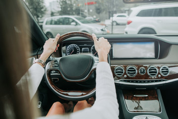 Close up woman hands keeping steering wheel while sitting in modern interior of vehicle. Girl...