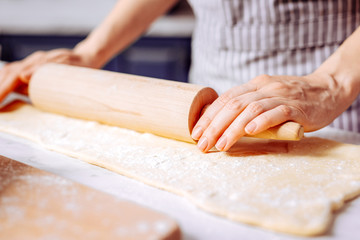 Hands on rolling pin. Calm young woman putting her two hands on the wooden rolling pin while wearing an apron and working with dough
