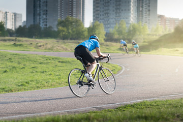 Active male athlete riding bicycles on an open asphalt road. Hills with green grass and the sunset