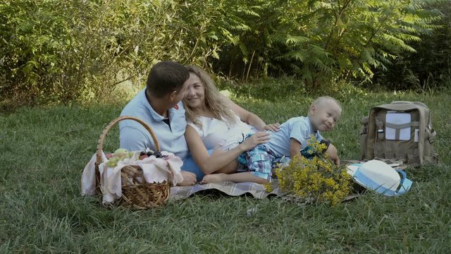 Happy family had a picnic in nature. Mom, dad and little son lie and play on the grass in the Park. Raw video. 4K. 25 fps.