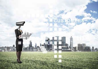 Camera headed woman standing on green grass against modern citys