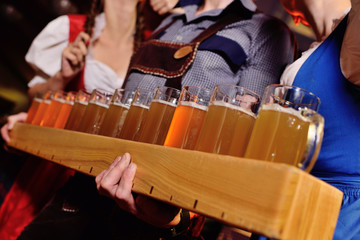 two attractive young girls and a man in traditional Bavarian clothes hold in their hands a lot of glasses of beer on the pub background during the celebration of the Oktoberfest