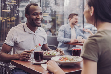 Enjoy your meal. Cheerful male person keeping smile on his face and looking at his friend