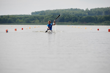 Fototapeta na wymiar Young sportsman competing on rowing competition, he paddling on his kayak on the lake